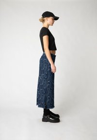 Svart kortärmad t-shirt, högmidjad denimkjol med vågmönster, fransad kant, matchad med svarta strumpor och kraftiga svarta skor.