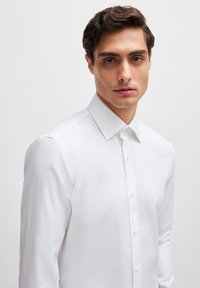 Witte lange mouwen shirt van gladde stof, met een klassieke kraag en knoopsluiting, in een getailleerde pasvorm en subtiele textuur.