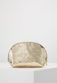 Guldmetallisk kosmetikpose med oval form, prægede diamantmønstre, lynlåslukning og rund dekorativ charm. Glat, skinnende tekstur.