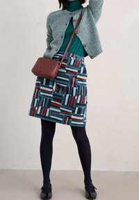 Knit cardigan in light blue, turtleneck in green, patterned skirt in navy with red and white accents, paired with dark tights and black shoes.