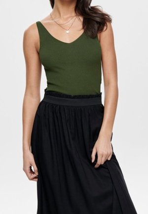 Femme portant un haut côtelé sans manches vert olive rentré dans une jupe plissée noire taille haute avec des colliers superposés.