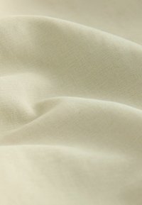 Närbild av mjukt, ljust beige tyg med subtil diagonalkonstruktion och mjuka veck som skapar en jämn textur och skuggor.