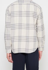 Lichtgekleurde geruiten shirt met grijze en witte strepen. Heeft een ronde zoom, lange mouwen en knoopmanchetten. Gemaakt van zachte stof.