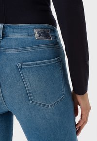 Světle modré džíny z denimu s jemným opraným vzhledem, mají zadní kapsu a značkovou koženou nášivku na pase. Hladká textura.