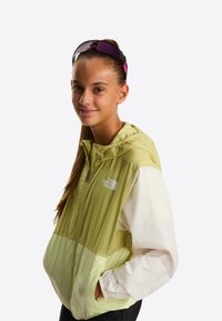 Letvægtsjakke med et markant mønster i lysegrøn og hvid, med hætte, lynlås foran og logo på brystet.