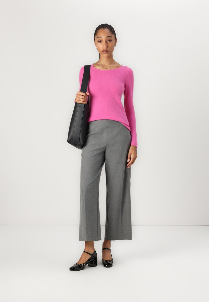 Rosa eng anliegender Pullover, graue weite Hose, schwarze Umhängetasche und schwarze Lacklederschuhe. Glatte Texturen und kontrastierende Farben.