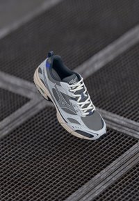 Grey running shoe with mesh panels, white laces, and a blue accent on the heel. Features a cushioned sole and structured design details.