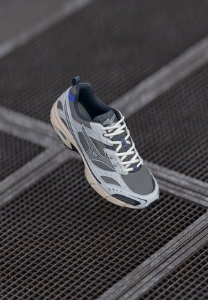 Grijze hardloopschoen met meshpanelen, witte veters en een blauwe accenten op de hak. Typt kenmerkend een gevoerde zool en gestructureerde ontwerpelementen.