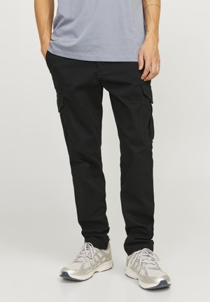 Pantalones cargo negros con bolsillos laterales, diseño ajustado, tela duradera, combinados con zapatillas deportivas grises que cuentan con una parte superior de malla y acentos blancos.