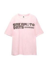 Lyserød bomulds t-shirt med fed sort tekst, der læser "SAKAMOTO DAYS" og japanske tegn; afslappet pasform, korte ærmer, rund hals.
