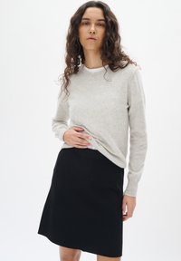 Pull gris clair en matériau doux, avec des manches longues et un col rond, associé à une jupe noire ajustée.