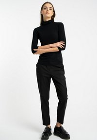 Czarny golf z rękawami trzyczwartowymi, zestawiony z luźnymi czarnymi spodniami i czarnymi masywnymi loafersami. Proste, jednolite kolory.