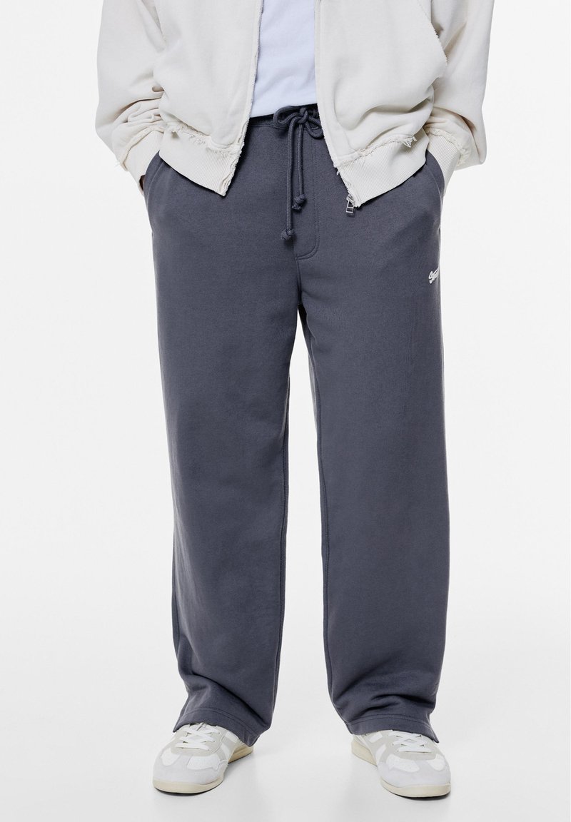 Donkergrijze sweatpants met een elastische tailleband en trekkoord. Soepele textuur, ruime pasvorm en klein merklogo op de bovenbeen.