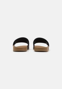 Sandales glissantes noires en matériau lisse, avec des brides larges et une semelle texturée marron. Présente un branding minimal sur le côté.