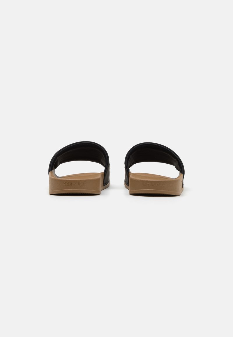 Sandales glissantes noires en matériau lisse, avec des brides larges et une semelle texturée marron. Présente un branding minimal sur le côté.