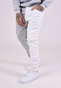 Joggers bicolor: un lado de denim gris claro y el otro lado de denim blanco. Presentan tobillos acampanados y se combinan con zapatillas blancas.