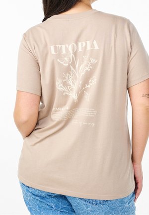 Beżowy t-shirt z botaniczną ilustracją, motylami i napisem "UTOPIA", noszony przez osobę widoczną od tyłu, w połączeniu z niebieskimi dżinsami.