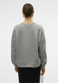 Sudadera gris con un ajuste relajado, hombros anchos y caídos, y puños acanalados. Tejido suave, costuras mínimas y sin patrones distintivos.