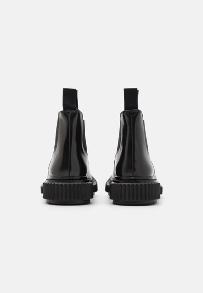 Botas de tobillo de charol negro con suela gruesa y estriada, paneles laterales elásticos y lengüetas en la parte posterior para facilitar su colocación.