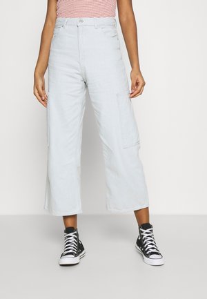 Person wearing light blue wide-leg cropped cargo pants and black high-top sneakers, standing against a plain background.