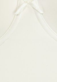 Débardeur blanc avec un tissu lisse et texturé, un col arrondi et un petit accent de ruban décoratif au niveau du col.