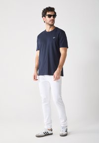 T-shirt à manches courtes bleu marine, jean blanc slim et baskets grises avec des rayures noires. Tissu texturé, design minimaliste.