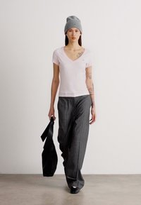 Ροζ μπλουζάκι v-neck, γκρι σκούφος, γκρι παντελόνι με ρίγες και φαρδιά γραμμή, μαύρη τσάντα, απλός σχεδιασμός, επίπεδα παπούτσια, μινιμαλιστική παλέτα χρωμάτων.