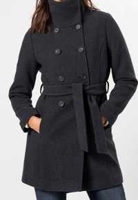 Abrigo de lana gris oscuro con un alto cuello, frente de doble botonadura, grandes botones, cintura ceñida con cinturón y bolsillos laterales. Textura suave y ajuste entallado.