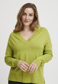 Pullover mit V-Ausschnitt und langen Ärmeln in leuchtendem Grün, aus weichem Strickmaterial mit gerippten Bündchen und Saum, mit einem lockeren Schnitt und seitlichen Schlitzen.