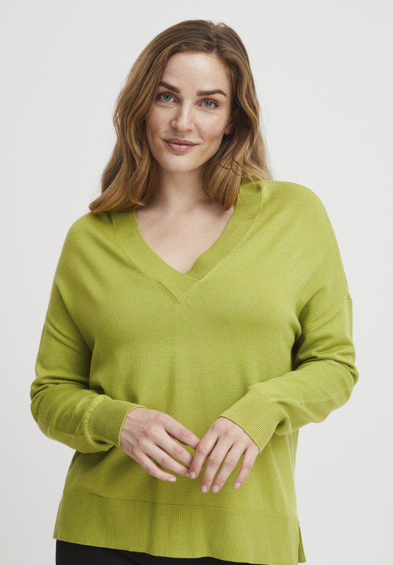 Pullover mit V-Ausschnitt und langen Ärmeln in leuchtendem Grün, aus weichem Strickmaterial mit gerippten Bündchen und Saum, mit einem lockeren Schnitt und seitlichen Schlitzen.