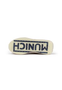 La suela de la zapatilla en goma color blanco roto presenta un logo azul "MUJNICH" y un patrón de agarre texturizado, destacando su durabilidad y tracción.