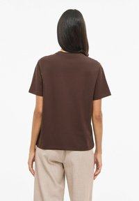 T-shirt marrone in cotone con maniche corte e vestibilità morbida, mostrata da dietro con una texture liscia e senza motivi visibili.