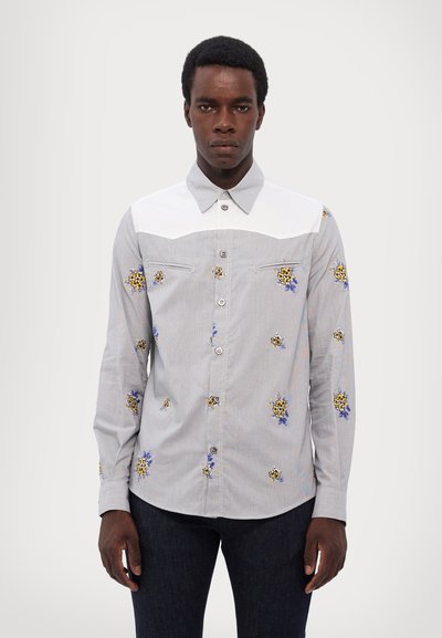 Camisa de manga larga abotonada en gris claro con yugo blanco, con bordado floral en amarillo y azul, y un cuello estándar.