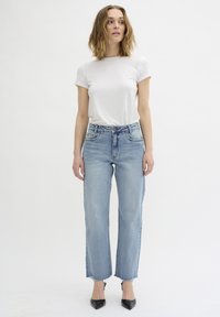 White short-sleeve t-shirt paired with light blue straight-leg jeans, featuring a raw hem and classic five-pocket design, complemented by black heels.