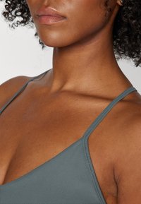 Gray ribbed fabric of a spaghetti strap top, featuring a smooth texture and a V-neck design, revealing shoulder and collarbone area.