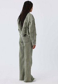 Chaqueta de mezclilla verde con estampado y pantalones a juego con bordes desgastados, que presentan un corte relajado y piernas anchas. Vista trasera que muestra la textura y los detalles.