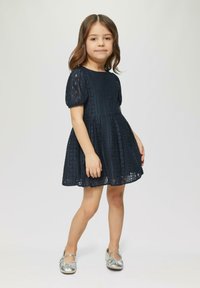 Marineblauw kantjurk met korte puff mouwen, een aansluitend lijfje en een uitlopende rok. Gecombineerd met glanzende zilveren ballerina's.