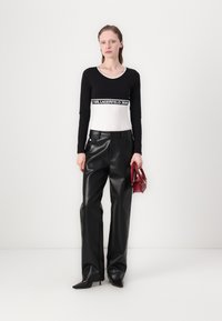 Black long-sleeve shirt with white base and logo band, paired with high-waisted black faux leather pants and a small red handbag.