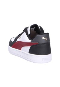 Zapatilla baja de Puma en blanco con paneles en negro y rojo, suela blanca y logo dorado de Puma en el talón.