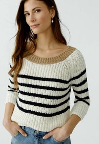 Le pull en tricot présente un large col côtelé beige, des rayures horizontales noires et blanches, et des manches trois-quarts. Tissu texturé.