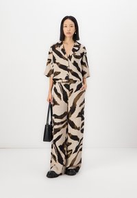Ensemble deux pièces comprenant une chemise légère à manches courtes et un pantalon large en beige avec un imprimé animal brun et noir.