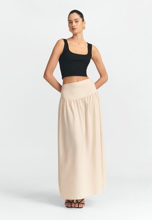 Čierny pruhovaný crop top v kombinácii s voľnou béžovou maxi sukňou s ručne zhromaždeným pásom. Model stojí v čiernych sandáloch na remienky.