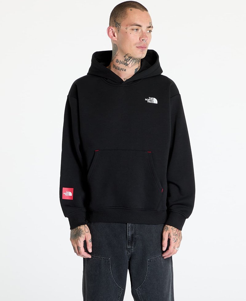Sudadera negra con bolsillo tipo canguro, con un pequeño logo blanco en el pecho y un acento rojo en el dobladillo. Material de algodón texturizado.