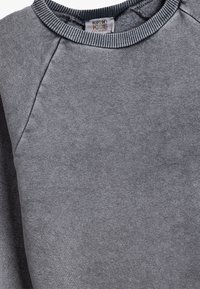 Grå sweatshirt i mjukt tyg, med ribbad rund halsringning och raglanärmar, med minimal sömnad och en etikett inuti.