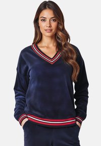 Felpa in velluto navy con scollatura a V, maniche lunghe e polsini a strisce rosse e bianche. Texture morbida con una vestibilità rilassata.