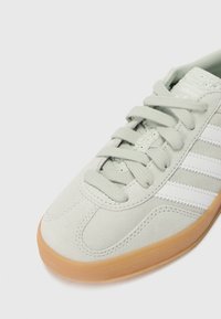 Gray suede sneaker with white stripes, textured laces, and a gum rubber outsole. Features rounded toe and stitched detailing.