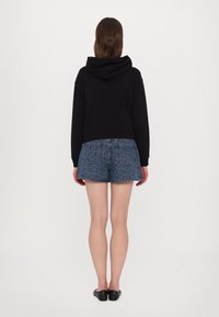 Svart cropped hettegenser med hette, kombinert med blå denimshorts med mønster. Shortsen har et geometrisk design og lommer.