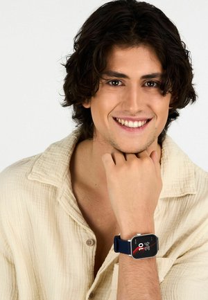 Smartwatch con quadrante rettangolare, cinturino in silicone blu scuro, display touchscreen che mostra l'ora e grafica, indossato su un polso.