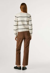 Crème trui met zwarte horizontale strepen, gecombineerd met bruine corduroy broek en zwarte stevige schoenen. Eenvoudig en functioneel ontwerp.