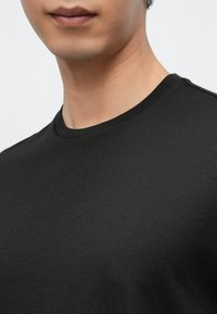 Čierne tričko s okrúhlym výstrihom z hladkej látky. Má jednoduchý dizajn s jednoliatou farbou a jemným prešitím pozdĺž výstrihu.